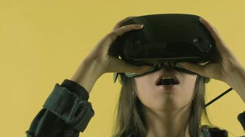 Young woman puts on vr headset, looks around and wonders how amazing in the VR world. Virtual reality helmet on the yellow background 3 video