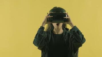 Young woman puts on vr headset, looks around and wonders how amazing in the VR world. Virtual reality helmet on the yellow background video