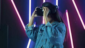 Young woman puts on VR headset and wonders how amazing in the VR world. Virtual reality helmet on color lighting background video