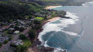 Aerial view of Hawaiian coastline and village, Scenic aerial view of a coastal village in Hawaii with lush greenery, ocean waves, beaches, and small homes along the shore. video