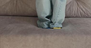 Women's blue jeans can be seen with yellow and blue socks resting on a soft sofa The close up captures a casual moment suggesting comfort and relaxation in a home environment video