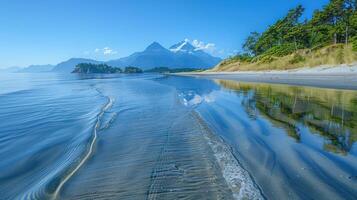 Tranquil beach scene with calm water reflecting mountains and trees. photo
