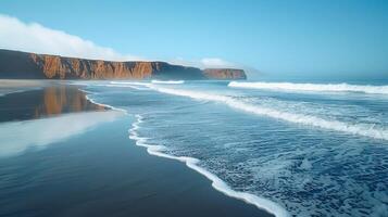 Calm beach scene with waves lapping onto shore, reflecting cliffs in calm water. photo