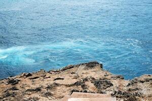 Beautiful landscape aerial view for cave on rocky cliff at the sea with foam waves and splash water. Travel destination seascape of summer calm ocean in Bali at Indonesia photo