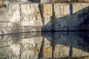 A large rock quarry is reflected in a pond photo