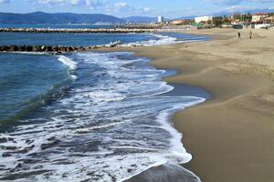 Sandy beach with gentle waves and a coastal town in the background. photo