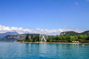 A Ferris wheel located on the shore of a picturesque lake surrounded by mountains and green trees. photo