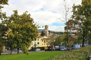 Photo of a cosy small town with traditional architecture, stone bell tower and green trees in the foreground.