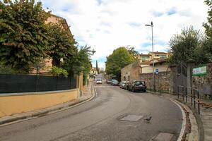 A quiet European street in a small town with parked cars, lush green trees and historic architecture. photo
