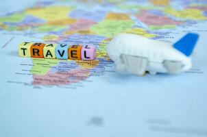 Small plastic cubes with text TRAVEL placed on world map with small airplane. Travel and exploration concept photo
