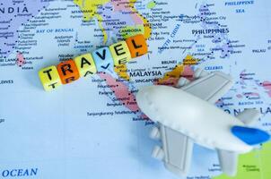 Top view of small toy airplane placed on a world map and plastic cubes with text TRAVEL. Travel and destination concept photo