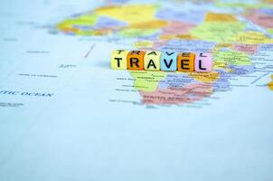 Small plastic cube with text TRAVEL placed on a world map representing travel or global exploration photo