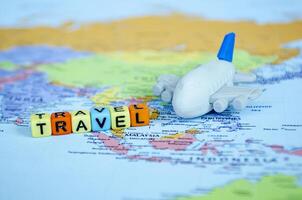 Small plastic cube with text TRAVEL and a small airplane placed on a world map representing travel or global exploration photo
