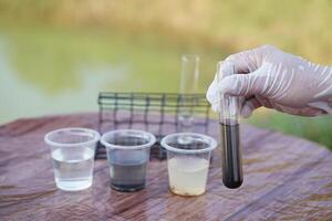 Scientist hand hold glass tube that contains sample of water to do science experiment. Concept Testing of water quality and contaminants from natural water sources photo