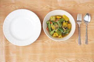 Bowl of curry mixed organic okra , pumpkin and Thai herbal ingredient. Empty plate, spoon and fork. Concept, local food with nutrient. Healthy eating. High fiber and vitamin. Top view shot photo. photo