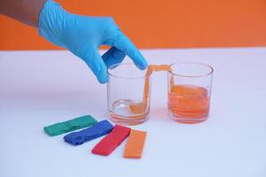 Hand holds glass of water and colorful stripes paper. Equipment for doing science experiment about chromatography. Concept, Easy activity chemistry lesson for kid. photo