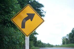 Yellow traffic sign with arrow right curve symbol beside the rural road to warn drivers to know the way ahead has right curve. Concept. Warning traffic sign for transportation. photo
