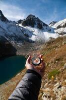 Man explorer looking for direction with compass in summer mountains, first person view of man hand with modern compass photo