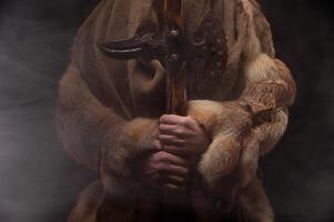 Medieval warrior berserker viking in leather with fur and an axe in his hands. Unrecognizable man in smoke stands fabulously mystically calmly photo