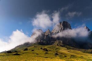 stunning view of sharp, jagged mountain peaks partially covered by clouds, with golden sunlight casting a warm glow on the rocky cliffs, creating a dramatic and awe-inspiring landscape photo
