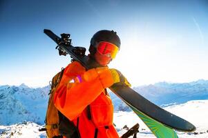 Portrait of young man with skis in snow at ski resort. Happy tourist relaxing on sunny day on top of mountain photo