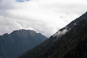Beautiful view of a valley in the mountains on a summer day with thick clouds and rays breaking through. Close-up of the curve of the hills covered with forest photo