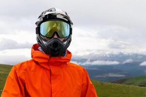 Modern motorcycle helmet with goggles on young guy standing in field with foggy mountains in background, portrait photo