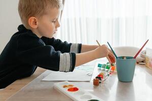 A young boy of European descent, around 4-5 years old, is engaged in painting at home. He mixes colors in a palette, experimenting with shades and enjoying the creative process photo