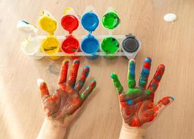 children's palms stained with paint, open cans of paint on the table, open palm of a child 4-5 years old photo above