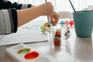 the boy takes acrylic paint with a brush from a can and starts to draw a circle on a piece of paper, the child draws with paints photo