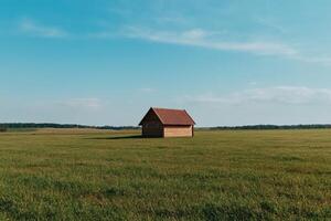 Small wooden cabin in a vast grassy field under a clear sky photo