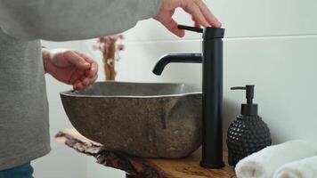 Man washing hands in stone sink with black modern faucet. Close-up of hand under running water in bathroom interior with stone basin video