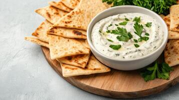 Creamy spinach dip served with pita chips and fresh herbs on wooden board photo
