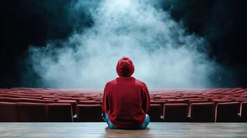 person in red hoodie sits alone in dark theater, surrounded by fog photo