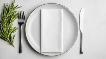 simple white plate with folded napkin, fork, and knife, garnished with fresh herbs photo
