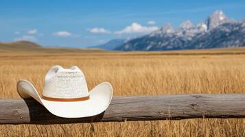 cowboy hat resting on wooden fence in golden field with mountains photo