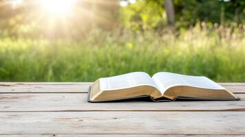 Freshly opened book on wooden table with sunlight shining through trees photo
