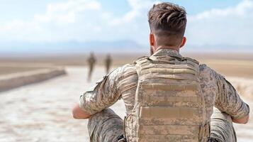 soldier sitting on path, observing fellow soldiers in distance photo