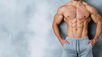 A man with a muscular body standing in front of a gray wall photo