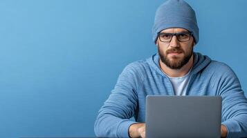 A man in a beanie and glasses is using a laptop photo