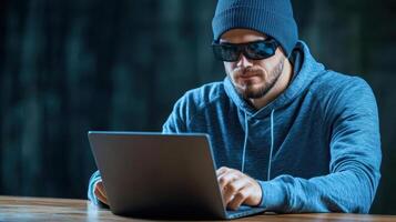 A man in a hoodie and sunglasses using a laptop photo