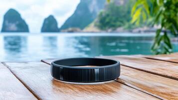 A black ring sits on a wooden table near the ocean photo
