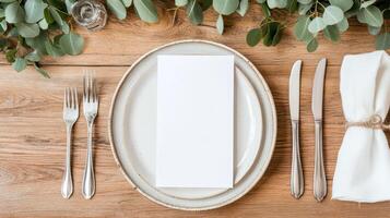 warm wooden table setting with blank menu, cutlery, and greenery photo