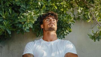 A man in a white t - shirt is leaning against a wall photo