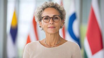 Professional woman with curly hair and glasses, standing confidently in front of flags photo