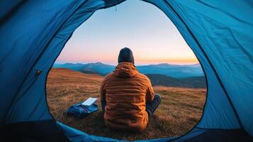 person enjoys serene sunset view from inside tent, surrounded by mountains and nature photo