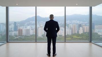 businessman suit stands by large window, gazing city skyline with mountains background photo