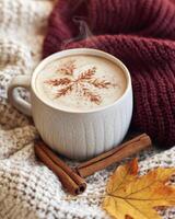 Cozy autumn setup featuring a steaming mug with a leaf design alongside warm wool and fragrant spices photo