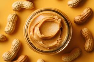 Peanut butter in jar surrounded by whole peanuts on yellow surface photo