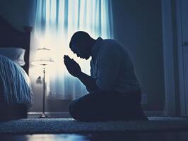 Man kneeling in prayer by a softly lit window at night photo
